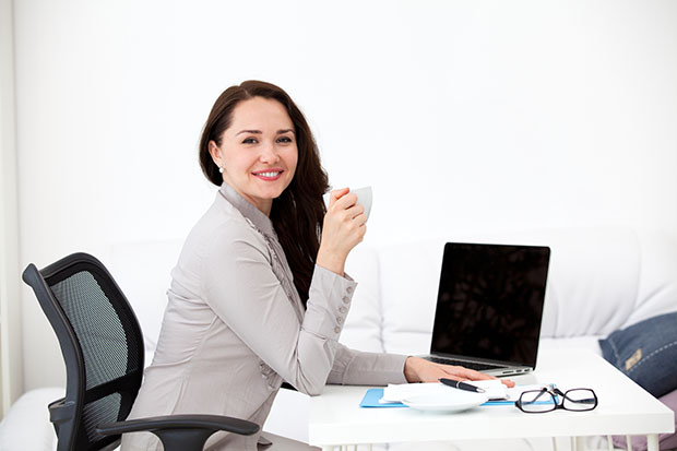 Businesswoman drinking coffee at desk, looking at camera, smiling in the office